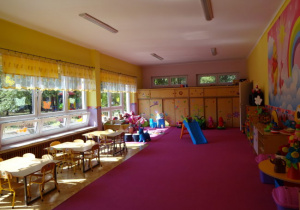przestronna sala grupy pierwszej ze stolikami i krzesełkami, różową wykładziną dywanową oraz wyposażeniem
