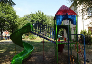 zestaw do zabaw ruchowych z domkiem i czerwoną zjężdżalnią oraz z dodatkową zieloną, zakręconą zjeżdżalnią na terenie ogrodu przedszkola