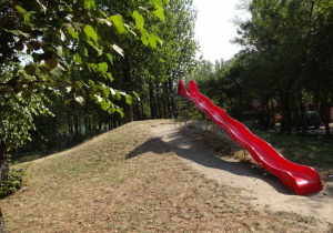 czerwona sześciometrowa pofalowana zjeżdżalnia zamontowana na górce w ogrodzie przedszkolaórce