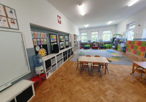 przestronna sala grupy piątej ze stolikami i krzesełkami dla dzieci, wyposażona w tablicę multimedialną