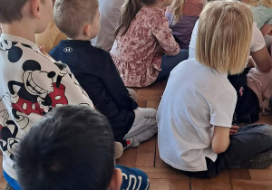 Grupa dzieci ogląda przedstawienie siedząc na podłodze.